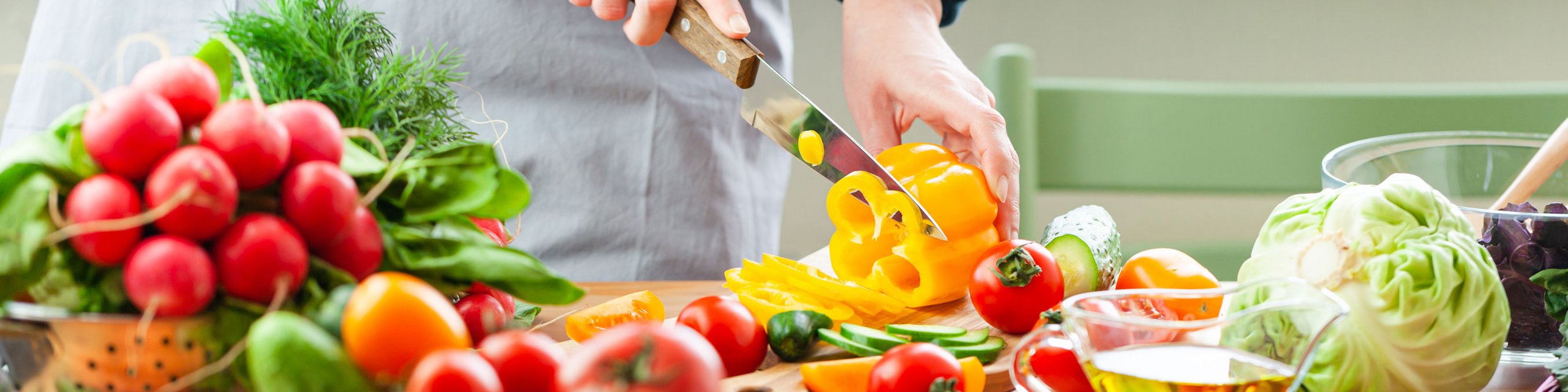 Eine Person schneidet eine Paprika. In der Küche liegt viel buntes Gemüse herum
