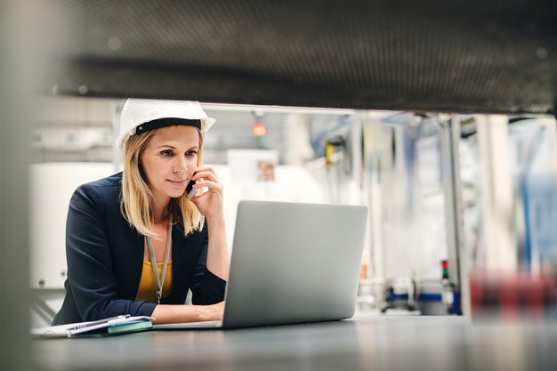 Frau mit Schutzhelm sitzt am Laptop und telefoniert
